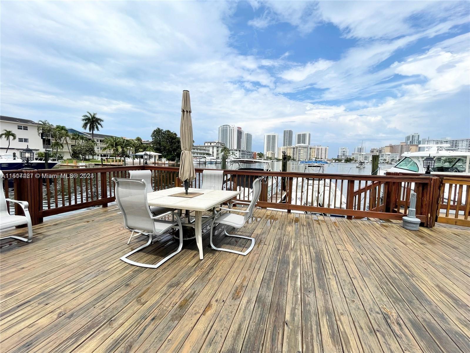 462 Golden Isles Drive, Unit 210 Hallandale Beach, FL 33009 - Photo 12 of 41 a view of a roof deck with table and chairs a barbeque with wooden floor and fence