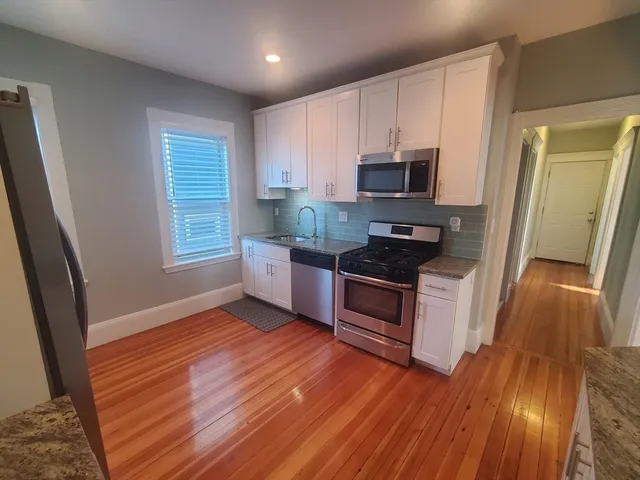 a kitchen with granite countertop wooden floors a stove and a microwave
