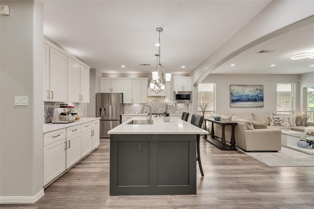 920 Sheldon Road Argyle, TX 76226 - Photo 6 of 36 Open-concept kitchen featuring an oversized island with seating, pendant lighting, stainless steel appliances, white cabinetry, and wood-finish flooring