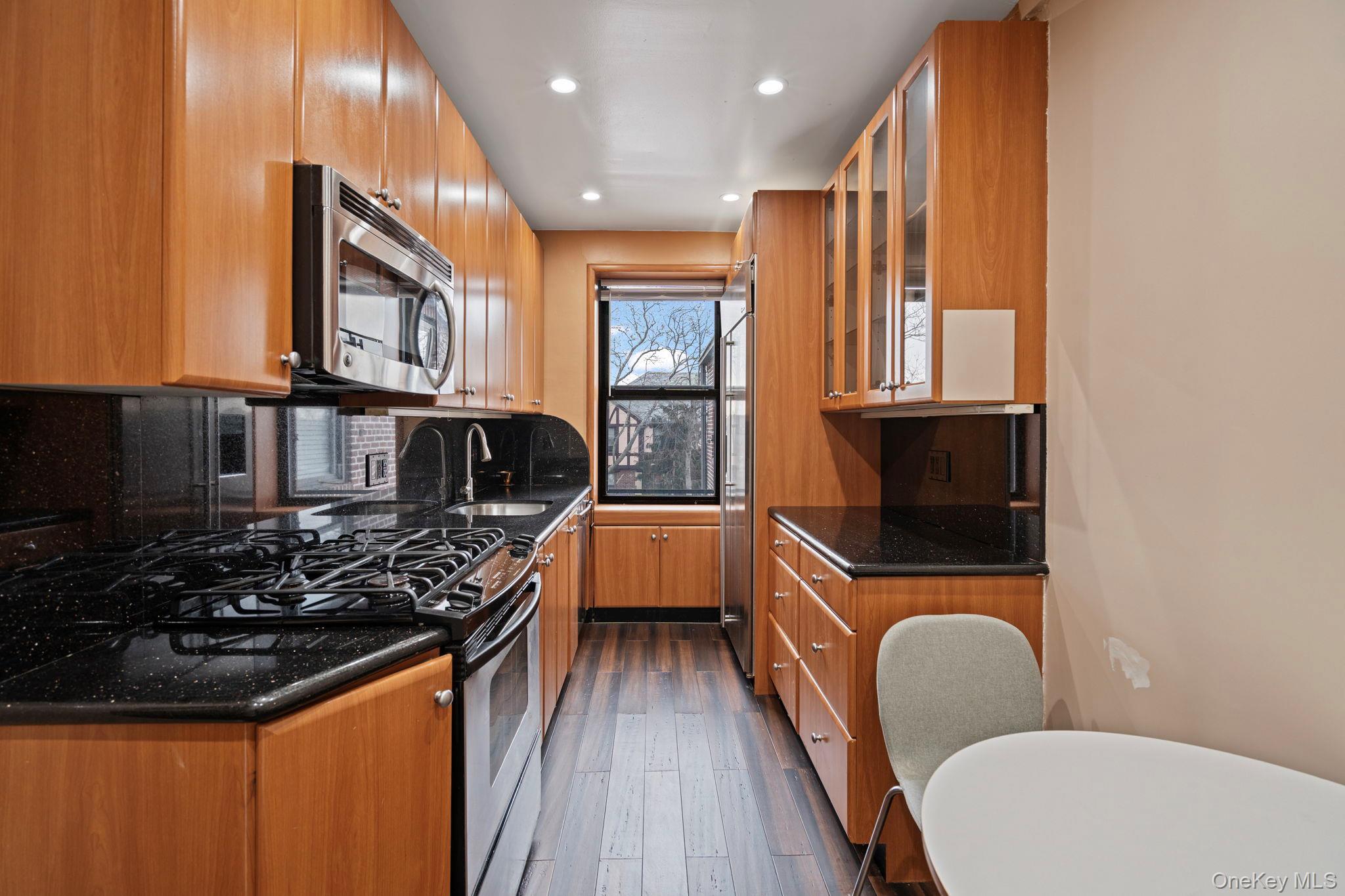 77-15 Ditmars Boulevard, Unit B2 Queens, NY 11370 - Photo 13 of 24 a kitchen with wooden cabinets a sink a stove and a window