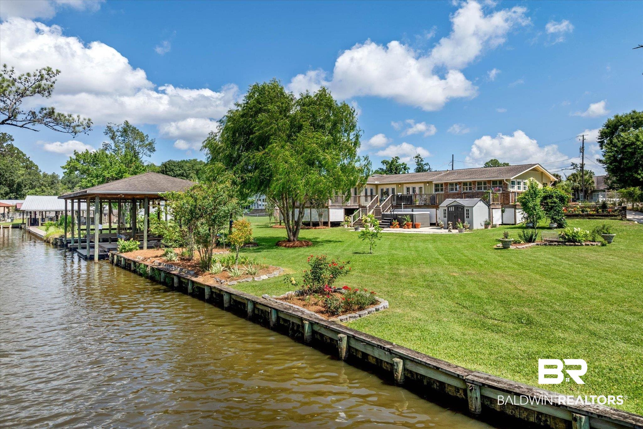 3801 Point Road Mobile, AL 36619 - Photo 2 of 55 Waterfront property featuring a covered boat dock, a wooden retaining wall, a spacious green lawn, multiple mature trees, and a multi-level wooden deck