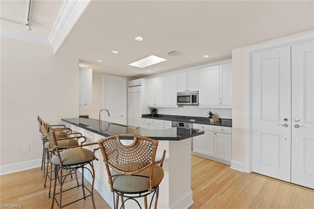 780 5th Avenue South, Unit 306 Naples, FL 34102 - Photo 13 of 31 a kitchen with stainless steel appliances granite countertop a stove top oven a sink a refrigerator with white cabinets and wooden floor