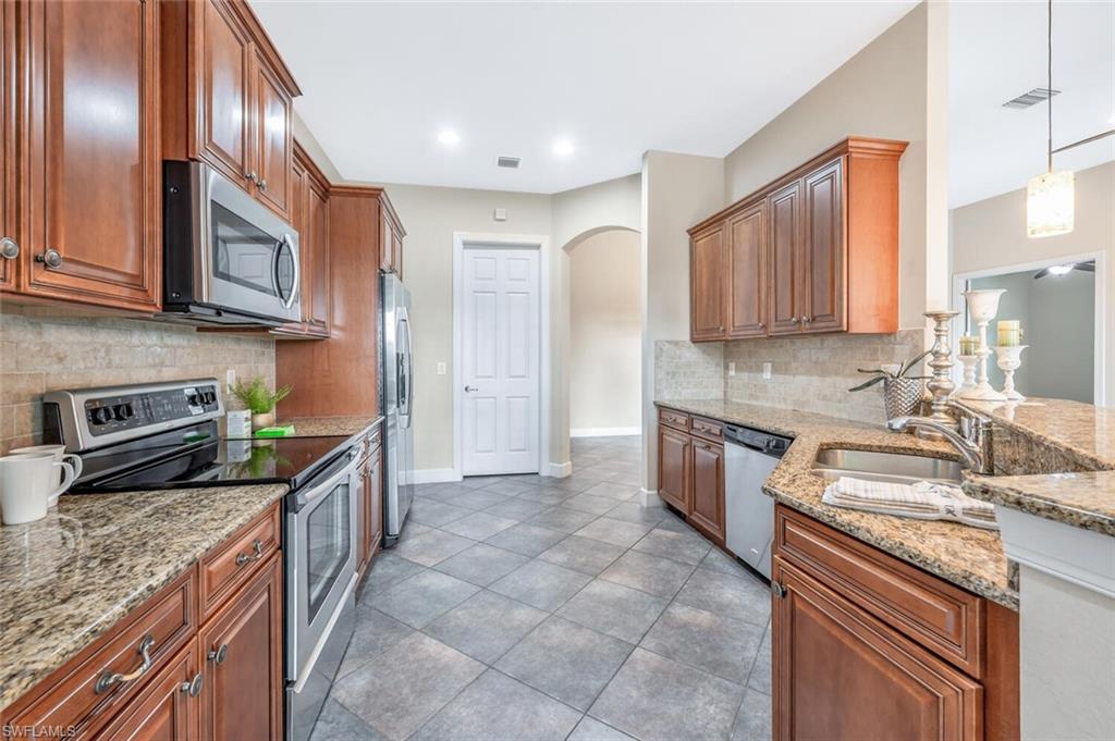 8237 Valiant Drive Naples, FL 34104 - Photo 6 of 35 Kitchen with appliances with stainless steel finishes, sink, tile patterned flooring, hanging light fixtures, and decorative backsplash