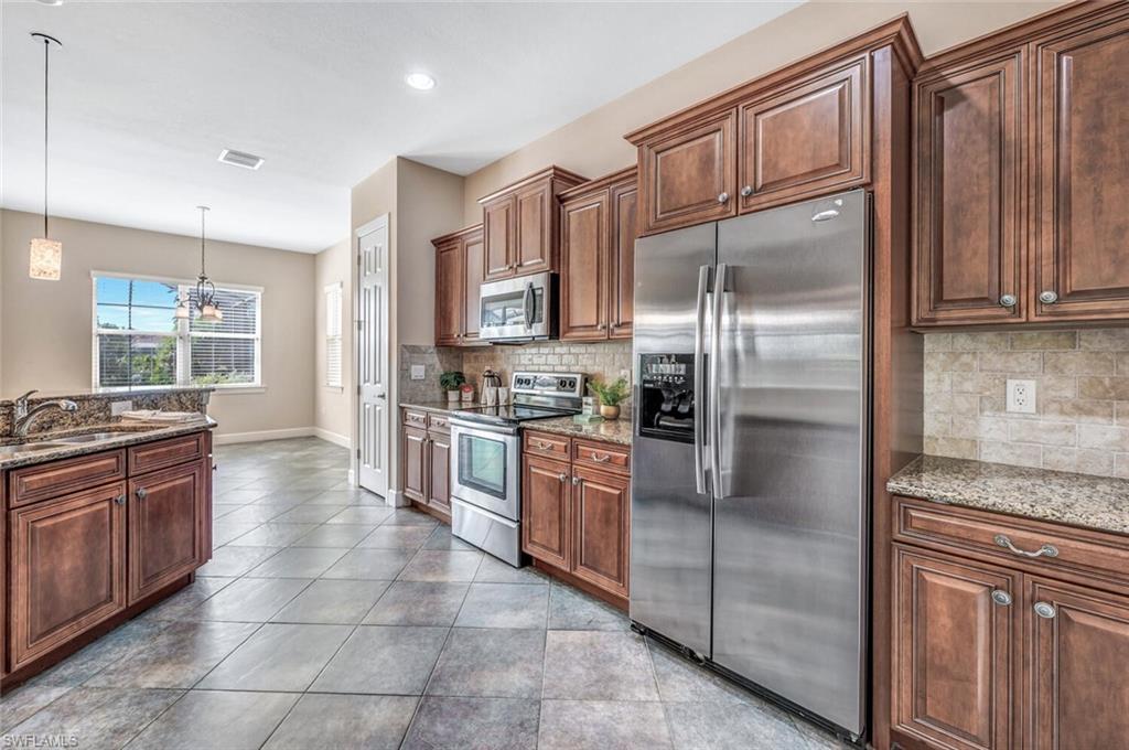 8237 Valiant Drive Naples, FL 34104 - Photo 7 of 35 Kitchen with stainless steel appliances, tasteful backsplash, sink, and stone countertops