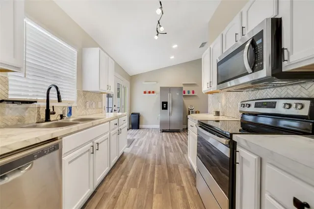 a kitchen with stainless steel appliances a sink a stove top oven a refrigerator cabinets and a dining table