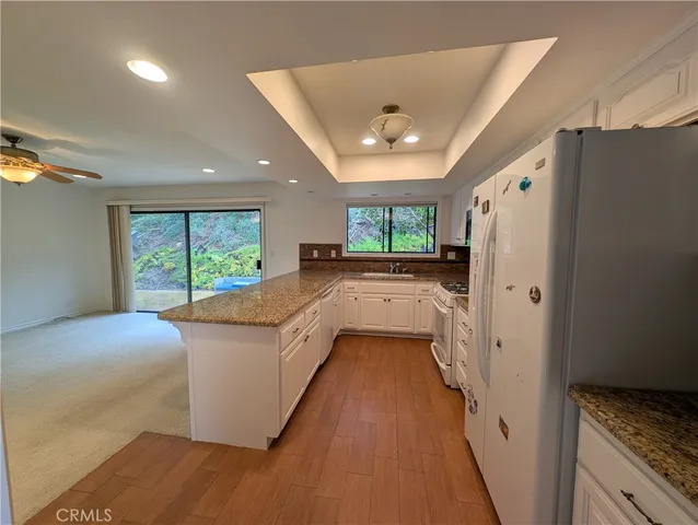 a kitchen with stainless steel appliances granite countertop a refrigerator a sink dishwasher a stove and a dining table with wooden floor