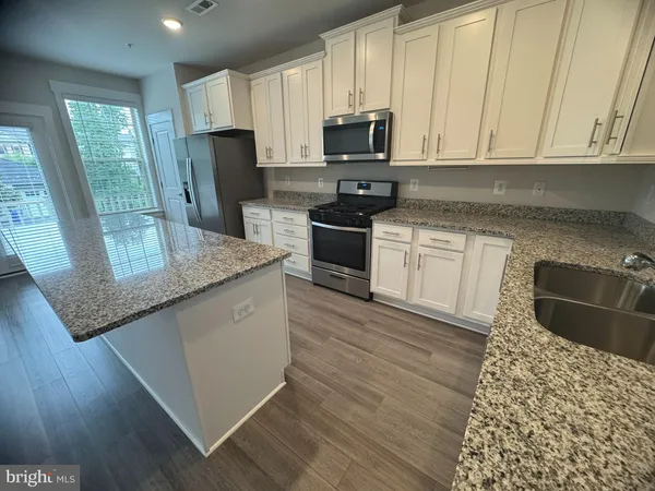 a kitchen with stainless steel appliances a stove a sink a microwave a refrigerator a cabinets wooden floor and a window