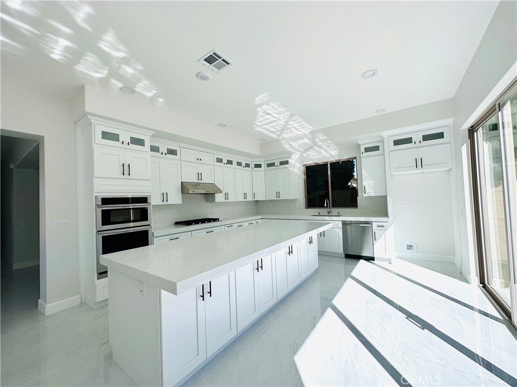 a large white kitchen with a stove top oven a sink dishwasher and a refrigerator with wooden floor
