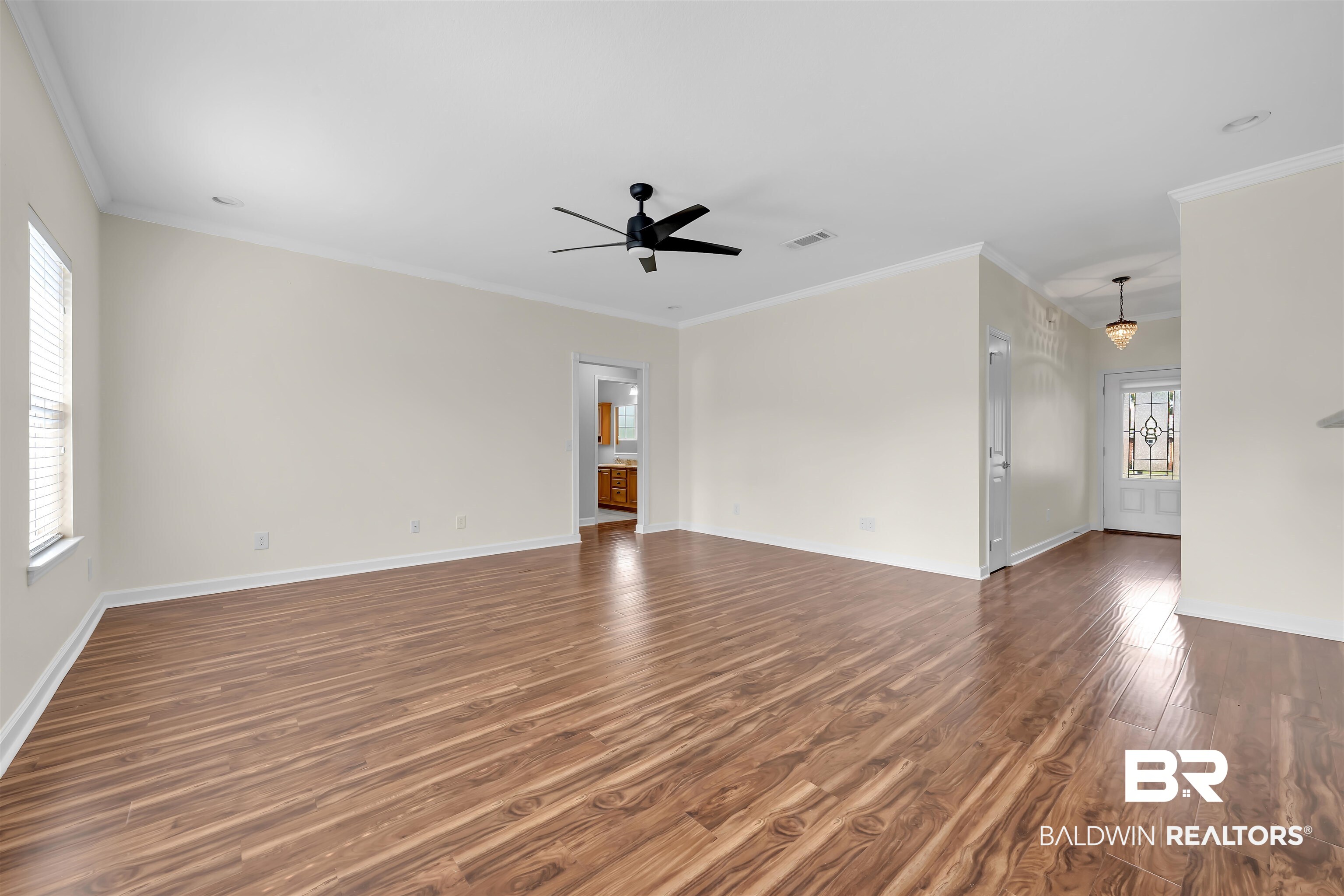 10147 Lyttleton Loop Lillian, AL 36549 - Photo 13 of 29 Open-concept living area featuring wood-finish flooring, a ceiling fan, a window with blinds, crown molding, and a decorative front door with leaded glass