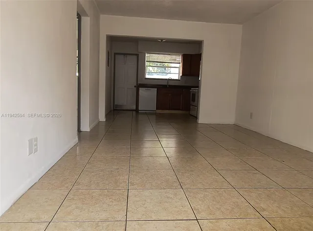 a view of an empty room with a window and a kitchen