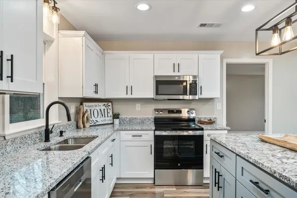 a kitchen with stainless steel appliances granite countertop a sink a stove and white cabinets