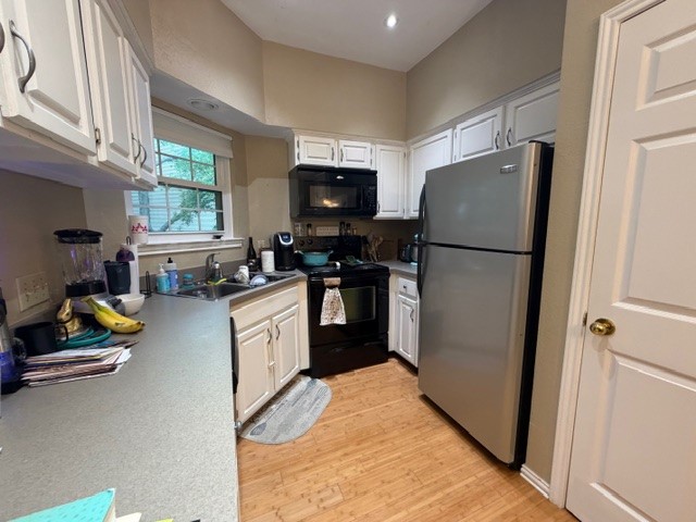 3809 Spicewood Springs Road, Unit 119 Austin, TX 78759 - Photo 5 of 14 The kitchen features white cabinetry, a stainless steel refrigerator, an oven with an overhead microwave, and a window above the sink