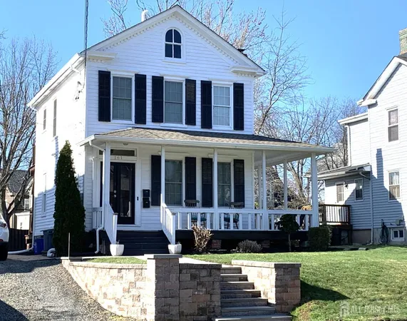 a view of a white house with large windows and a yard with plants and large trees