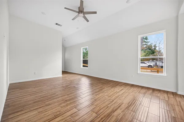 an empty room with wooden floor chandelier fan and windows