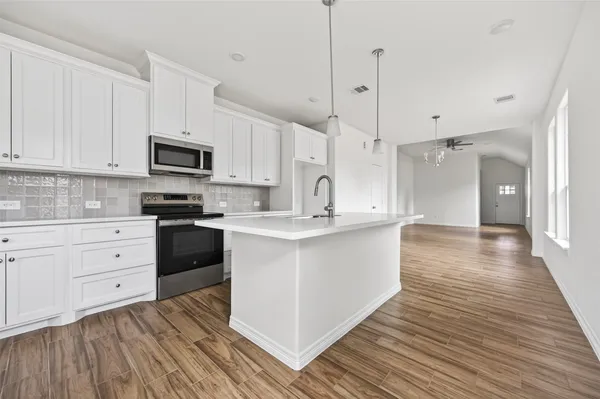 a kitchen with stainless steel appliances granite countertop a stove a sink and white cabinets with wooden floor