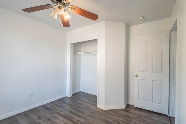 an empty room with wooden floor closet and windows fan