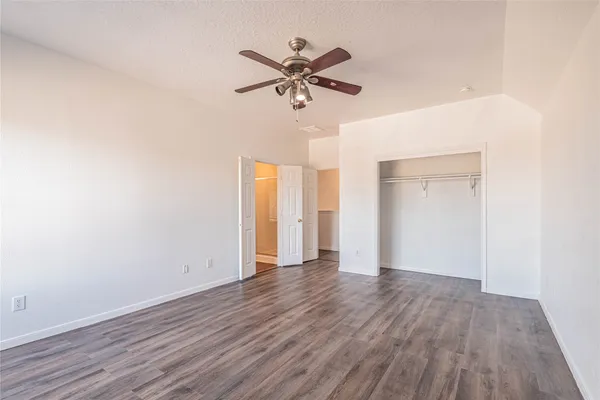 a view of an empty room with wooden floor and a ceiling fan