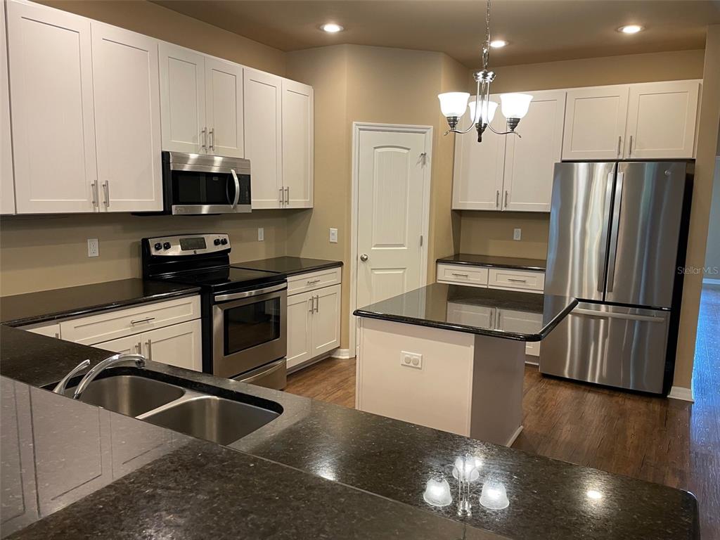 7879 Southwest 80th Drive Gainesville, FL 32608 - Photo 2 of 23 a kitchen with granite countertop a refrigerator a sink a stove and white cabinets with wooden floor