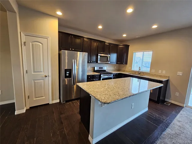 a kitchen with stainless steel appliances granite countertop a refrigerator a sink a stove and a wooden floors