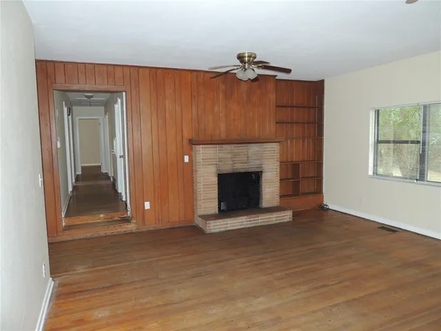a view of an empty room with wooden floor fireplace and a window