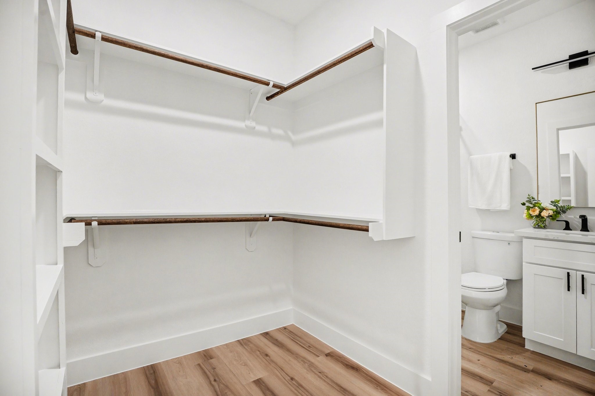 115 Milby Street Houston, TX 77003 - Photo 20 of 28 This photo shows a spacious walk-in closet with wooden flooring and ample shelving. It connects to a modern bathroom featuring a toilet, vanity, and fresh decor.