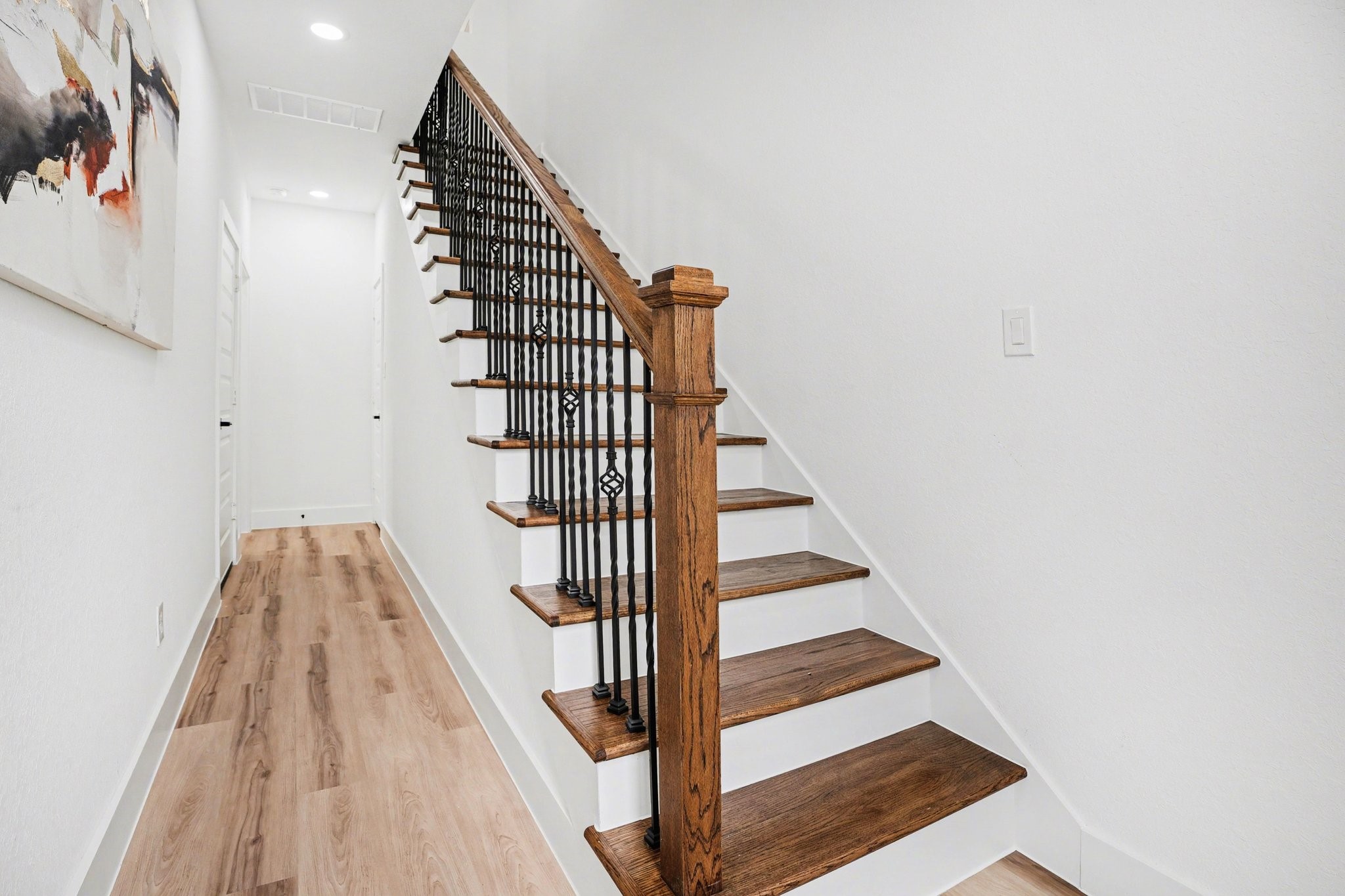 115 Milby Street Houston, TX 77003 - Photo 2 of 28 A bright, modern hallway featuring a wooden staircase with elegant iron balusters. The light wood flooring complements the white walls, creating a clean and inviting space.