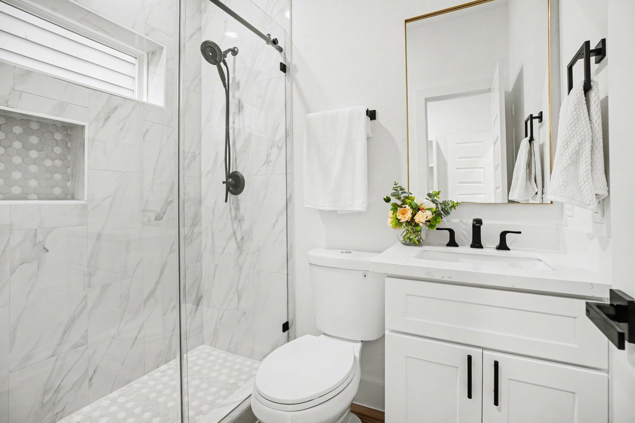 115 Milby Street Houston, TX 77003 - Photo 21 of 28 This bathroom features a modern design with a glass-enclosed shower, marble-style tiles, and a built-in niche. It includes a sleek vanity with black fixtures and a large mirror, offering a clean and elegant look.