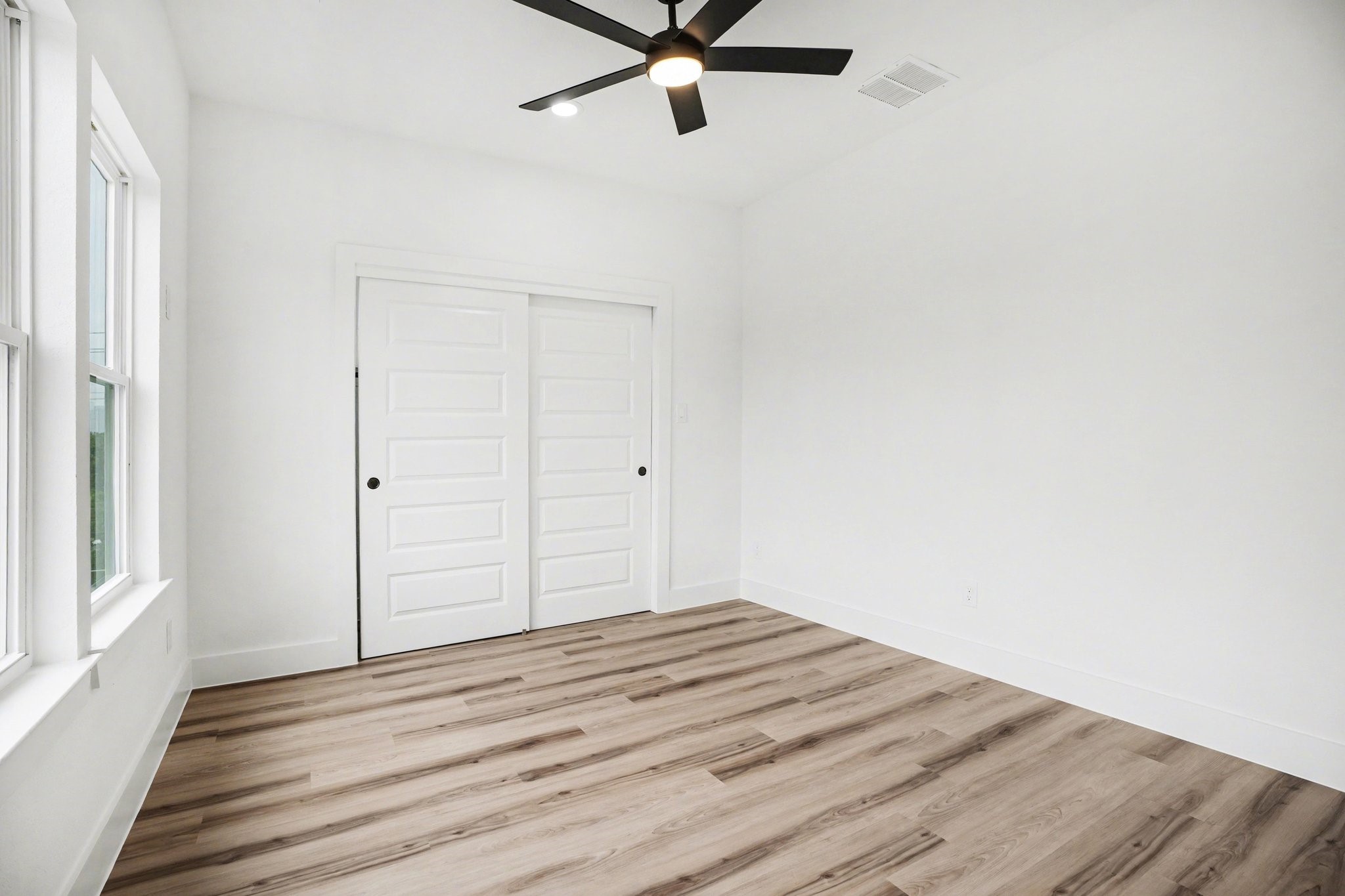 115 Milby Street Houston, TX 77003 - Photo 23 of 28 Bright and airy room with large windows, modern ceiling fan, wood-style flooring, and a double sliding door closet. Perfect for a bedroom or home office.