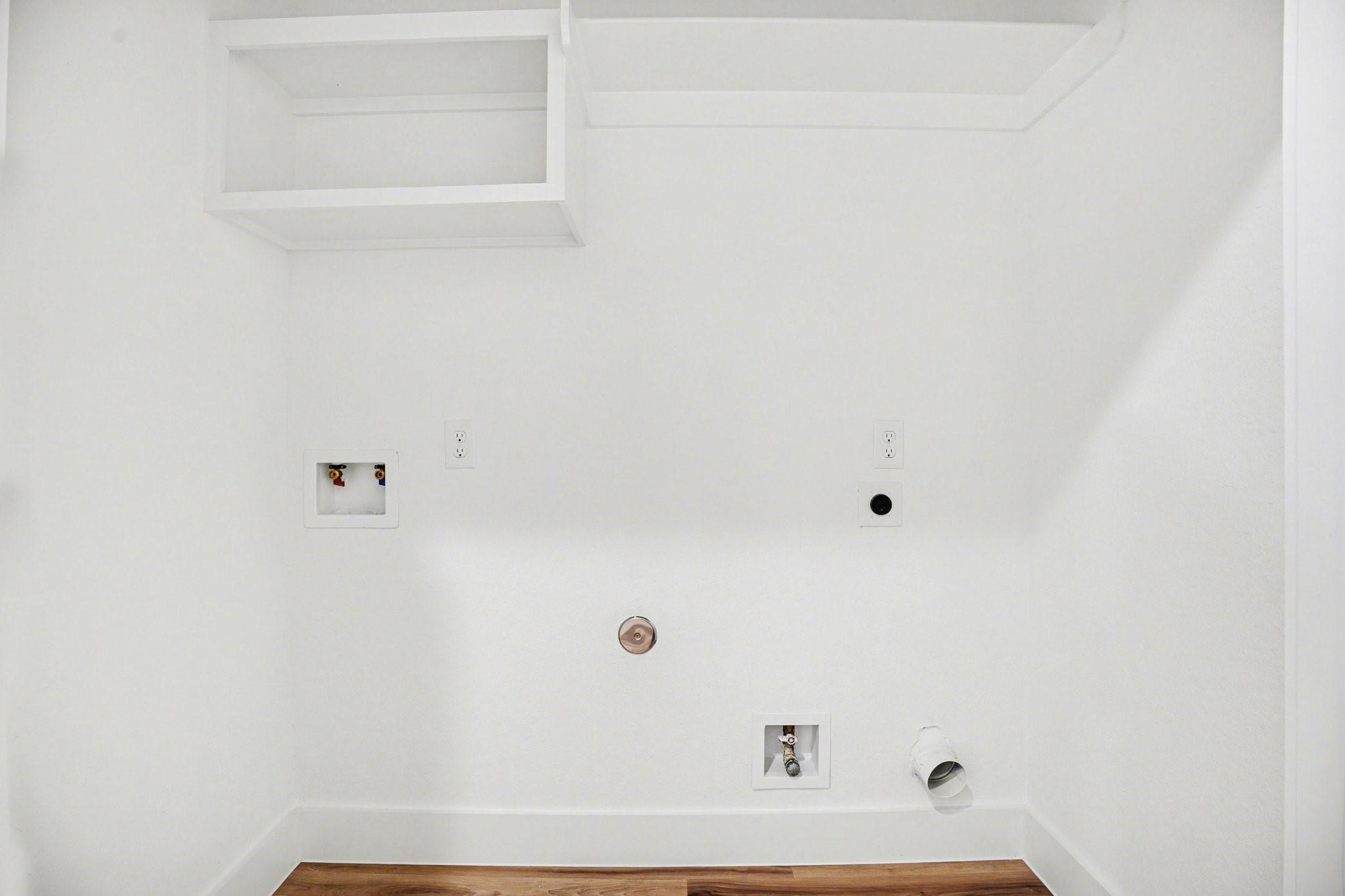 115 Milby Street Houston, TX 77003 - Photo 26 of 28 This photo shows a laundry area with hookups for a washer and dryer. It features white walls, an overhead shelf, and wood flooring.