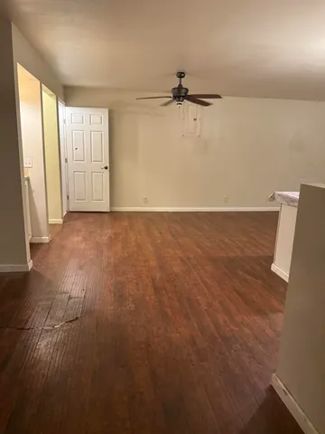 an empty room with wooden floor and kitchen view