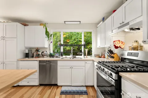 a kitchen with a stove a sink dishwasher and white cabinets with wooden floor