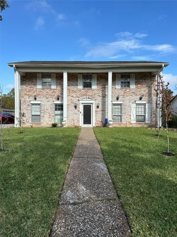a view of a house with brick walls and a yard with a large tree