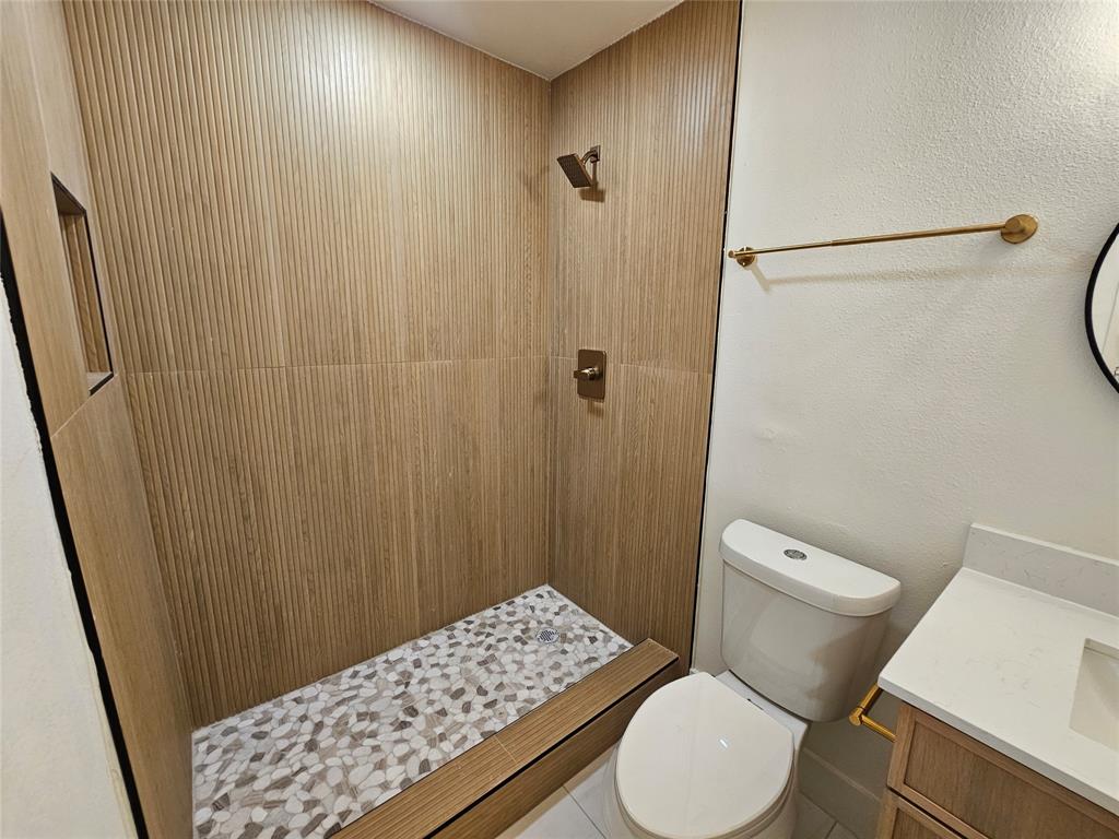 1725 R Avenue, Unit 1727 Plano, TX 75074 - Photo 10 of 20 Walk-in shower with textured wood-finish wall tile, pebble-style floor, and bronze fixtures