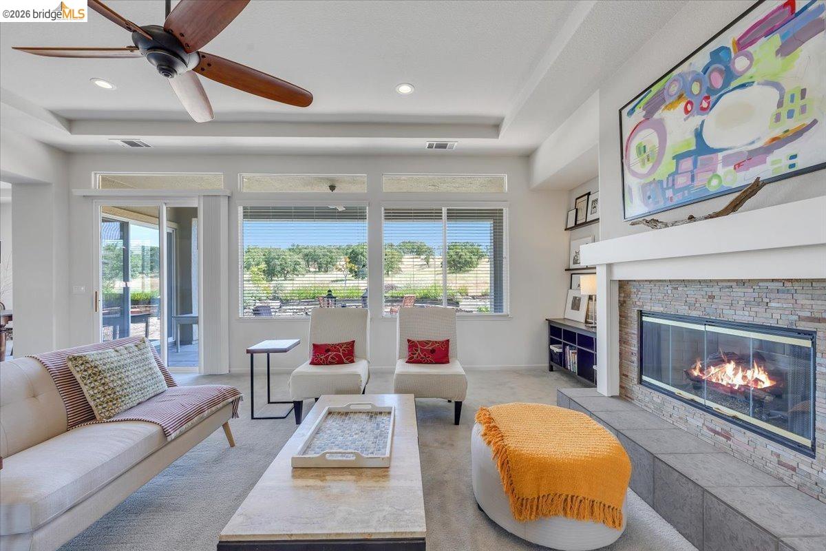 258 Rock Ridge Lane Copperopolis, CA 95228 - Photo 23 of 47 Living room featuring a stone fireplace, a ceiling fan, light colored carpet, and a raised ceiling