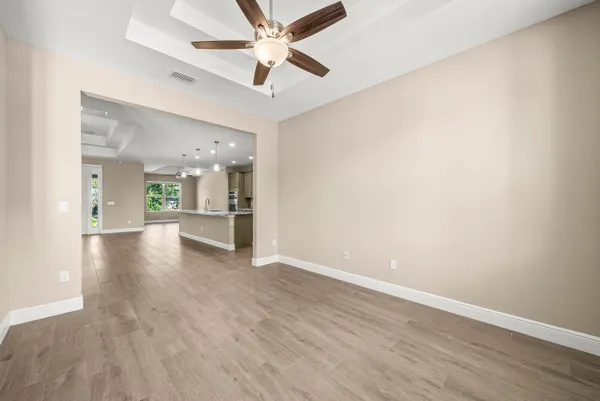 an empty room with wooden floor a ceiling fan and kitchen view