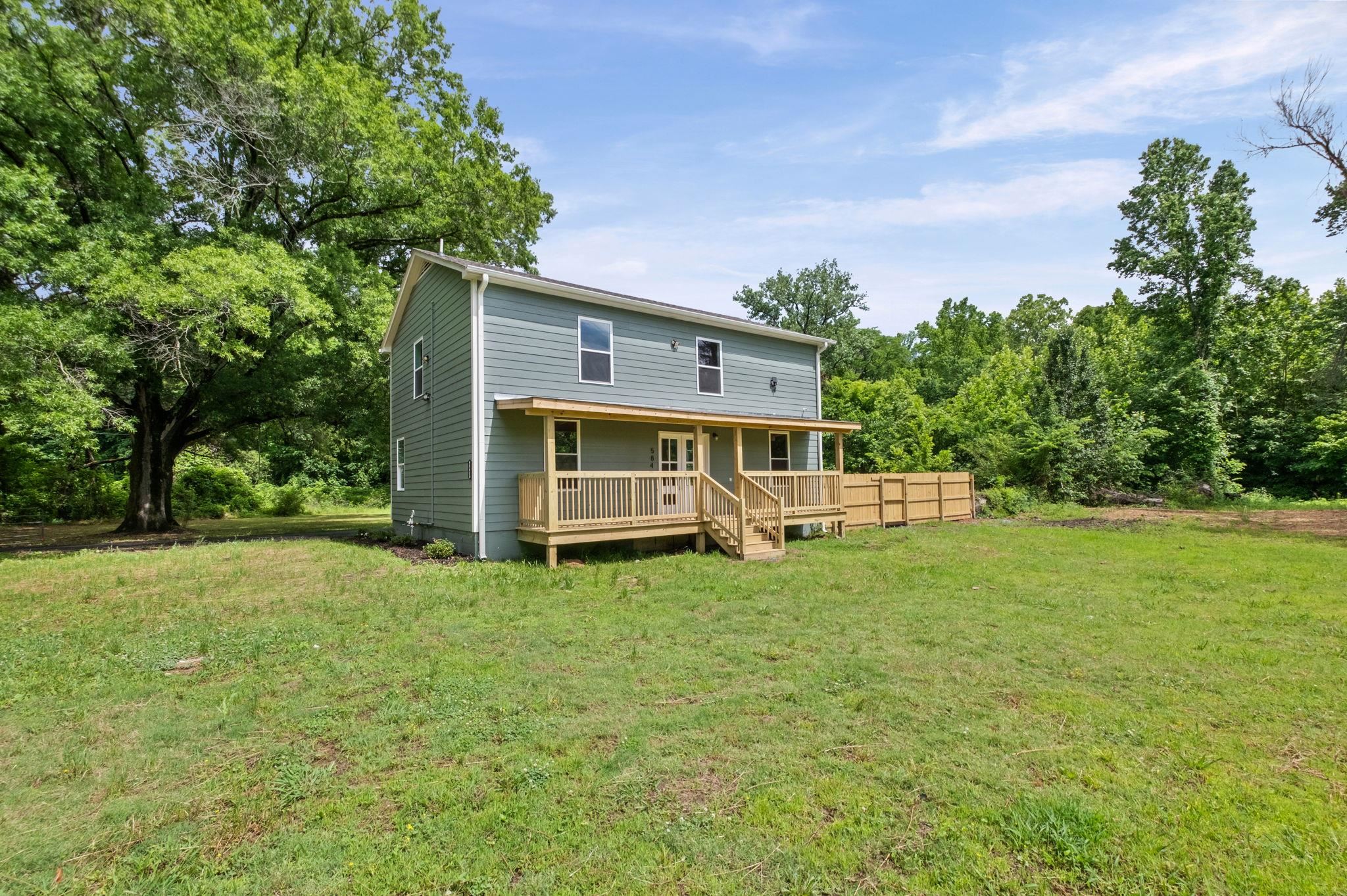 5843 Stewart Road Lakeland, TN 38002 - Photo 1 of 26 Two-story residence with light blue siding, a covered wooden porch, and a surrounding green lawn