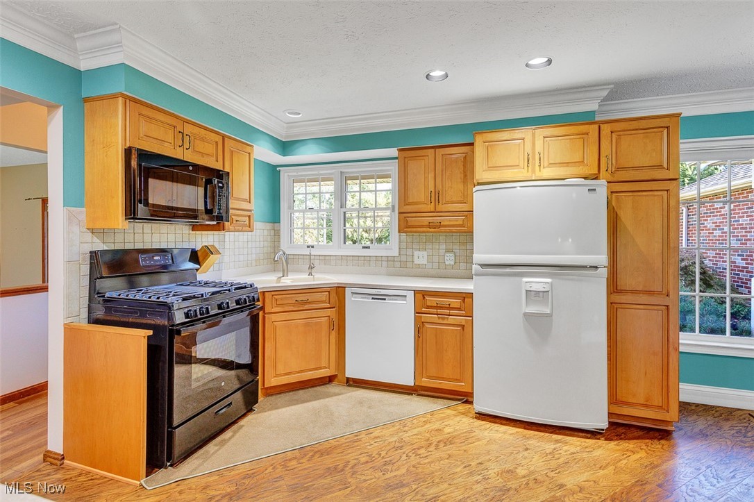 Kitchen featuring appliances, light countertops, light wood-style flooring, ornamental molding, and a textured ceiling