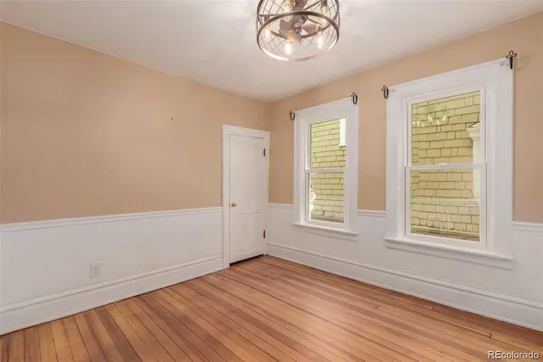 an empty room with wooden floor chandelier fan and windows