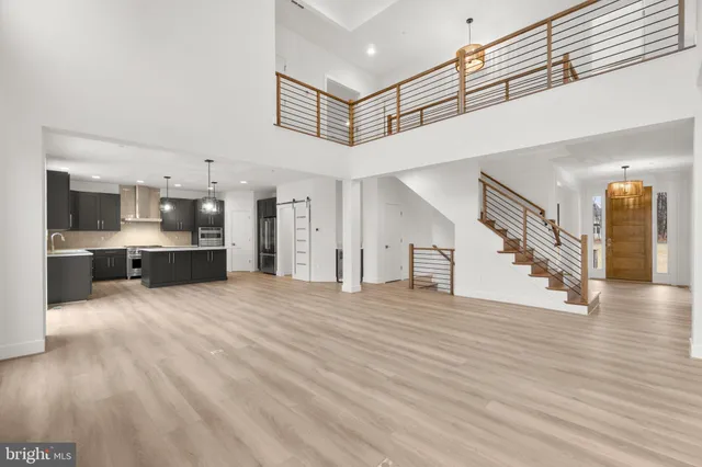 a view of an empty room and kitchen view with wooden floor