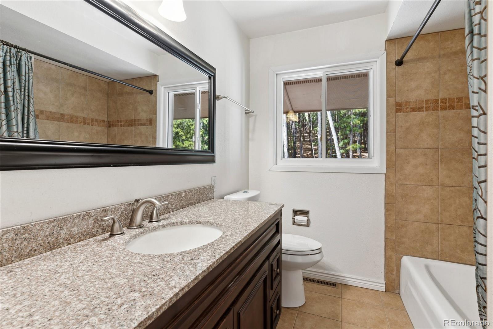 10807 Timothys Drive Conifer, CO 80433 - Photo 25 of 39 a bathroom with a granite countertop sink a toilet a mirror and shower