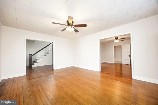 an empty room with wooden floor ceiling fan and windows