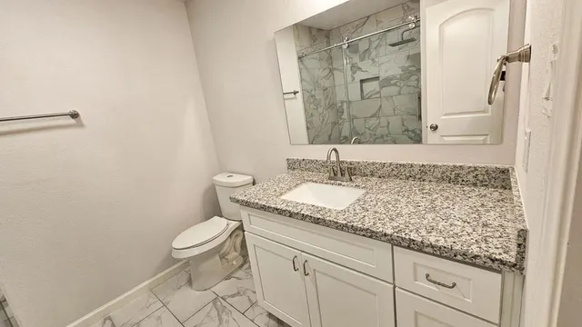 a bathroom with a granite countertop sink a toilet and a mirror
