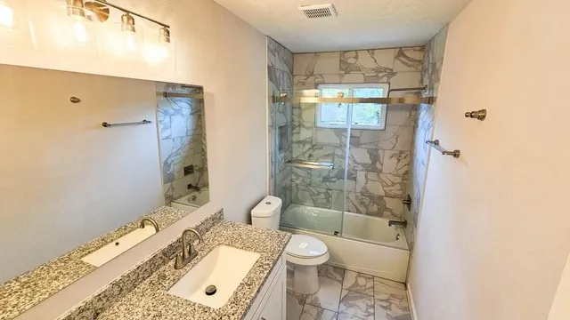 a bathroom with a granite countertop bathtub shower sink mirror and toilet