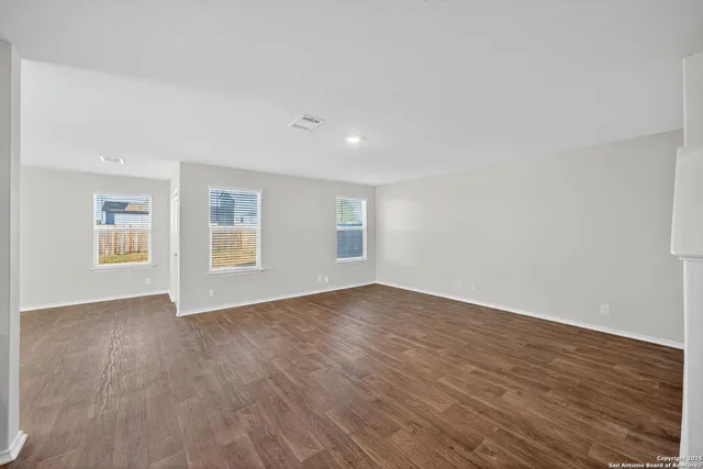 a view of an empty room with wooden floor and windows
