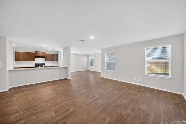 a view of kitchen and empty room with wooden floor and windows