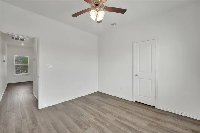 an empty room with wooden floor chandelier fan and windows