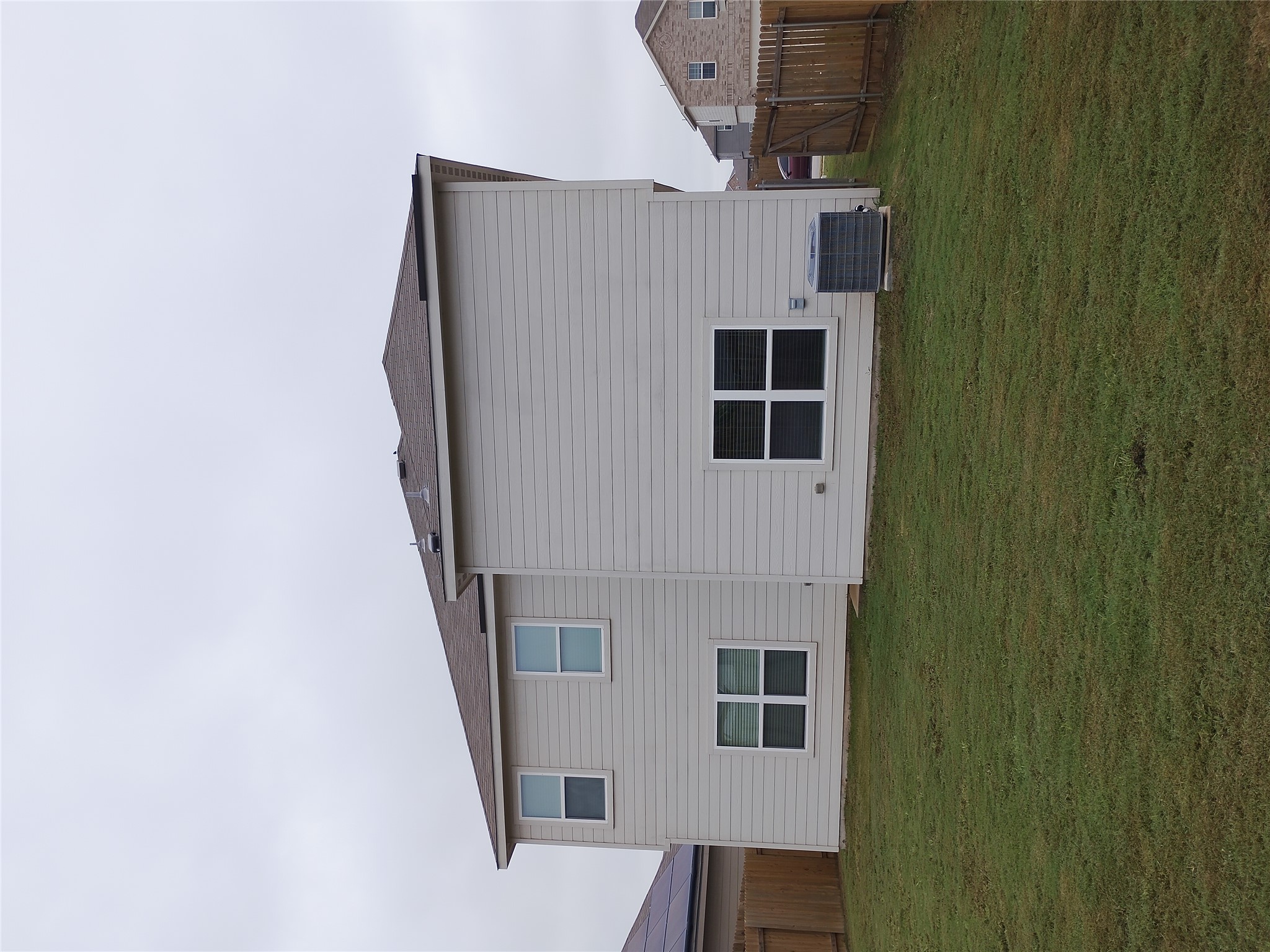 14024 Prairie Schooner Pass Elgin, TX 78621 - Photo 4 of 20 Spacious backyard with a grass lawn, featuring a multi-story home exterior with horizontal siding, multiple windows, and a shingled roof