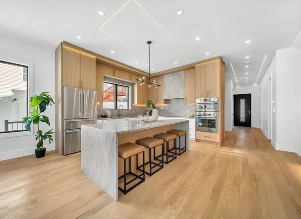 a large white kitchen with stainless steel appliances granite countertop a stove a sink a refrigerator and a dining table with wooden floor