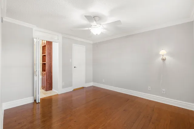 a view of an empty room with wooden floor and a ceiling fan