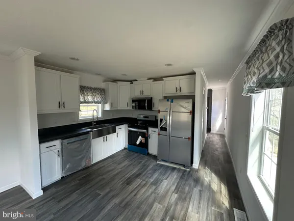 a kitchen with stainless steel appliances granite countertop a refrigerator a sink dishwasher a stove and white countertops with wooden floor